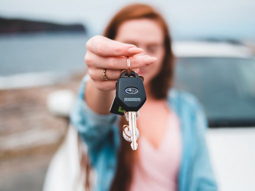 Set of keys in focus with woman and car blurred in background.