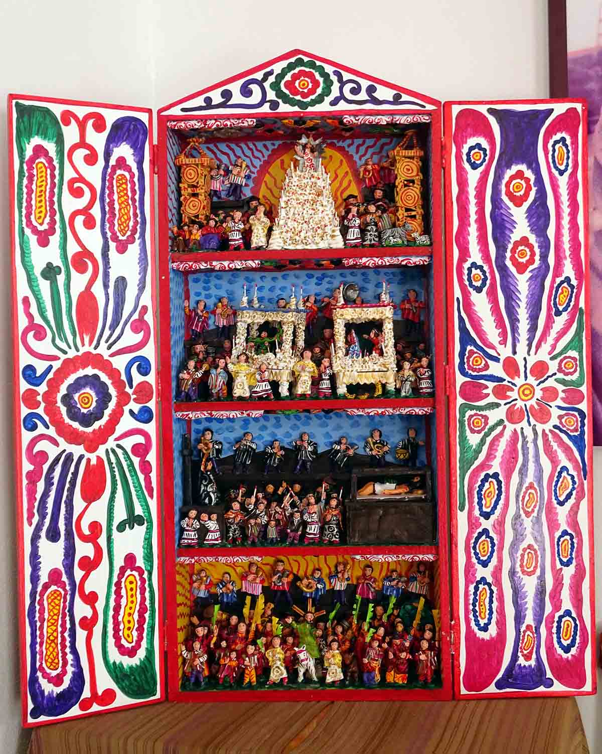 An altar-like retablo with colorful hand-painted designs on the doors and hand-carved figures inside