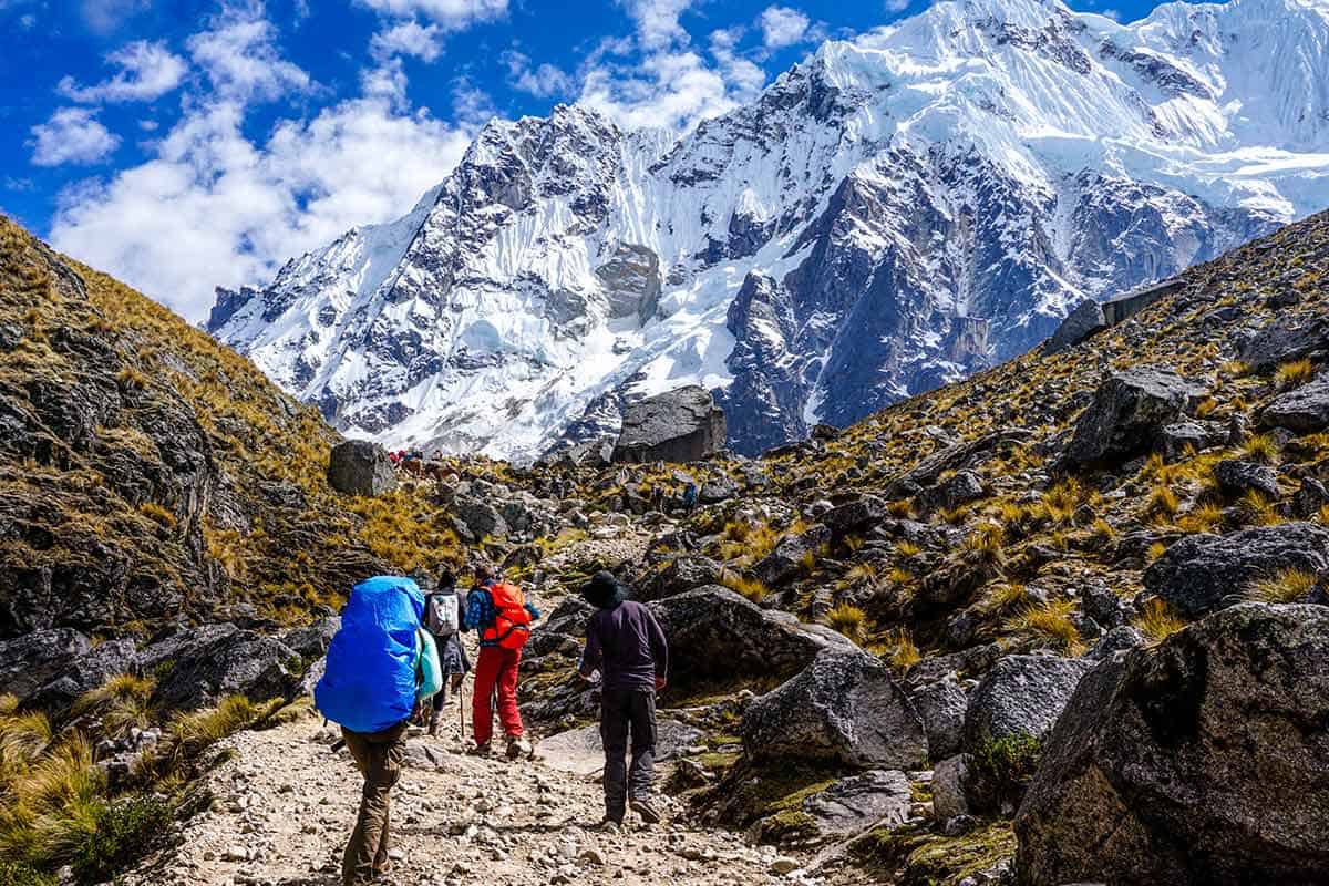 Trekkers wearing backpacks making a steep climb up a trail towards the snowcapped peak of Salkantay.