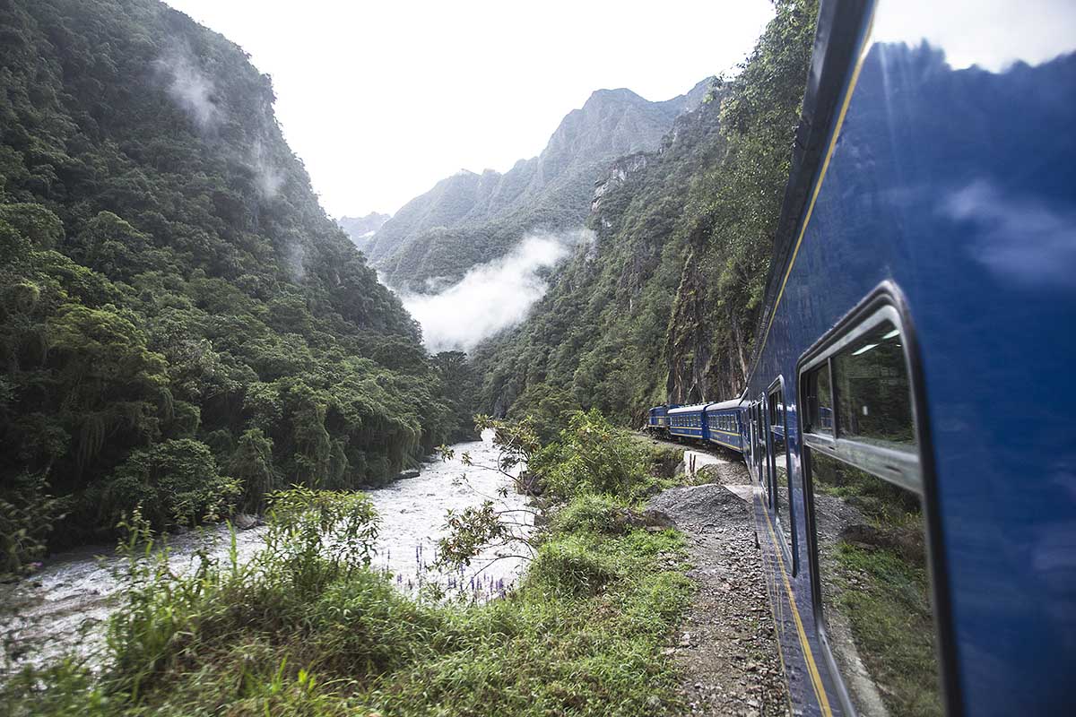 Machu Picchu train on the railway tracks along a river surrounded by lush mountains.