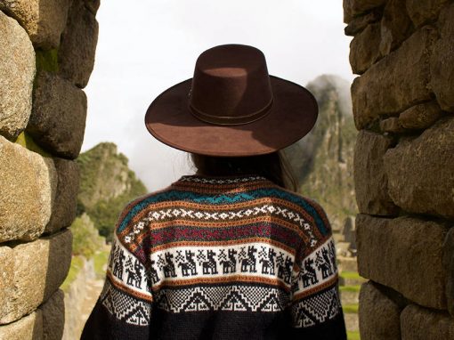 A woman wearing an alpaca sweater looking through a stone doorway at the ruins of Machu Picchu.