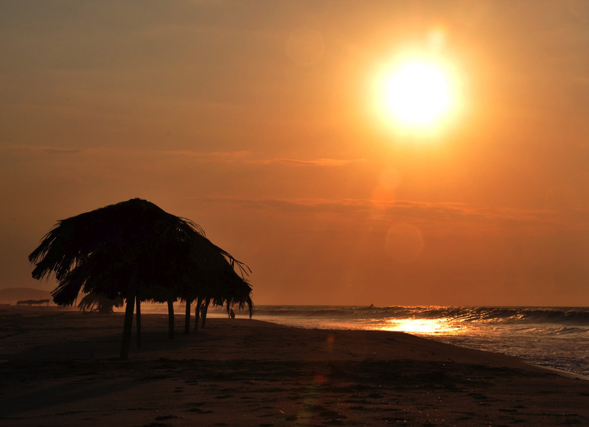 Cloudless orange sky at sunset with silhouette of straw beach umbrella at Los Zorritos, Peru.