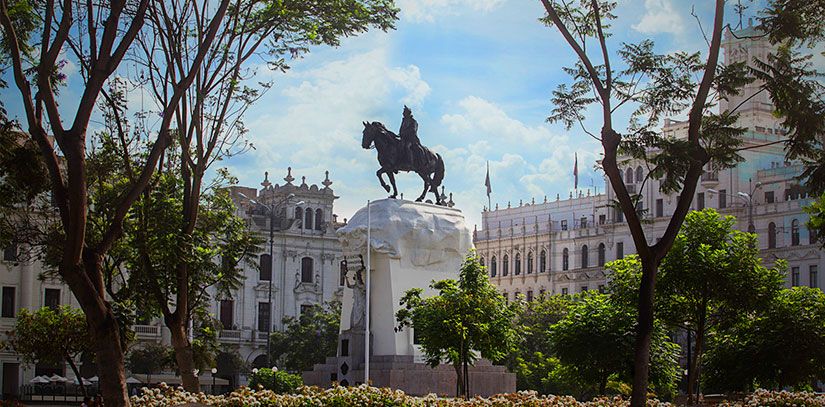Plaza de Armas in center of Lima on a mostly sunny day with trees, colonial government palacas and a man on horse statue