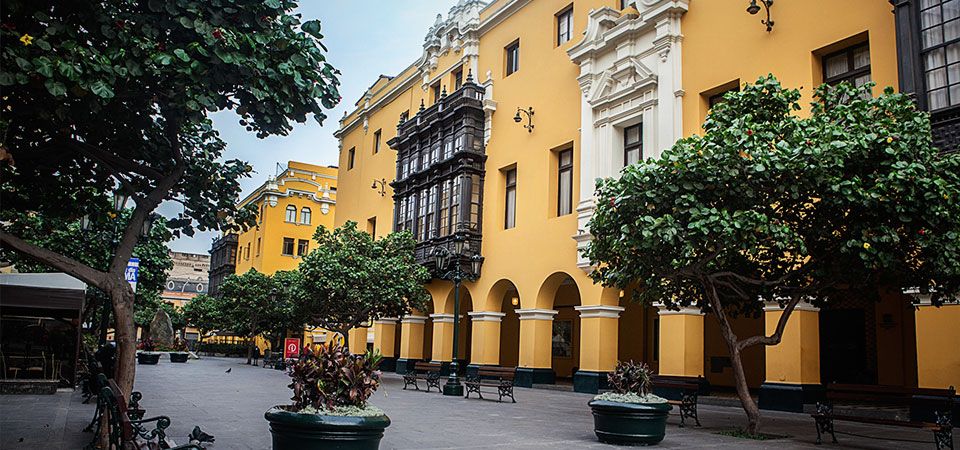 Yellow buildings displaying colonial architecture on a quiet street with trees in the historic district of Lima